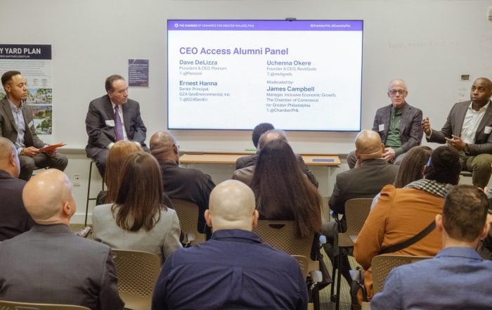 Speakers sitting panel style in front of a small crowd speaking